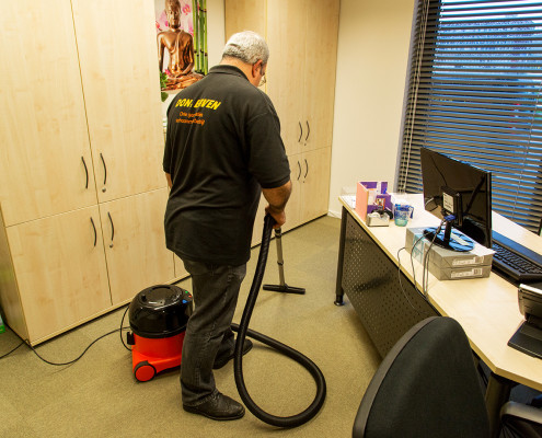 Schoonmaakbedrijf Bussum: werknemer die kantoor stofzuigt met stofzuiger